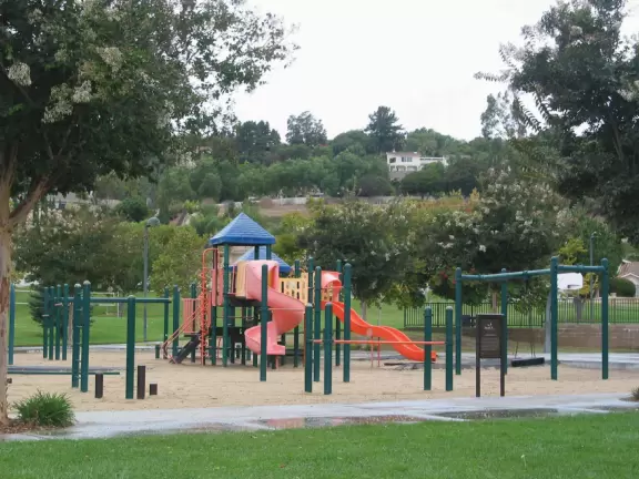 A park with flowering trees, cute playground, basketball courts, volleyball net, and mountain views.